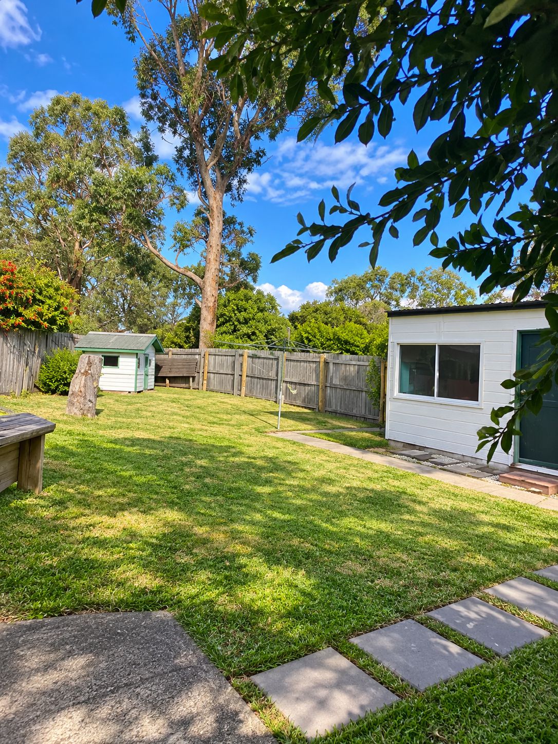 A backyard with a grassy lawn, a wooden deck, a small shed, and a house with a window.