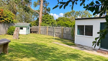 A backyard with a grassy lawn, a wooden deck, a small shed, and a house with a window.
