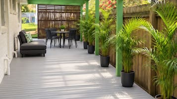 A covered patio area with a wooden deck, a seating area with a sofa and chairs, and potted plants.