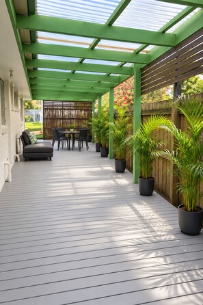 A covered patio area with a wooden deck, a seating area with a sofa and chairs, and potted plants. - Berwick Tweed - Peace and comfort (Melbourne)