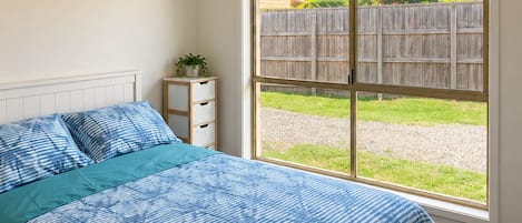 A bedroom with a large bed, a window, and a view of a backyard.
