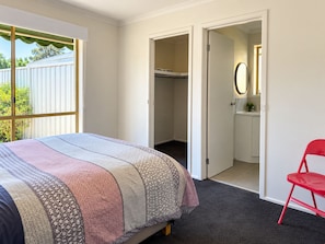 Un dormitorio con una cama, una silla roja y un vestidor.