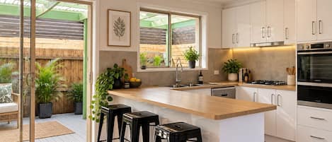 A modern kitchen with a wooden island, bar stools, a built-in oven, and a large window.
