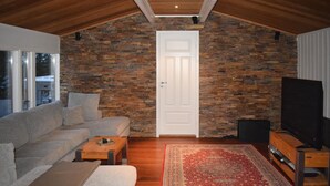 Ein Wohnzimmer mit einer Steinwand, einer weißen Tür, einem grauen Sofa, einem Couchtisch, einem roten Teppich und einem Fernseher auf einem Holzboden.