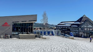 Ein Skischulgebäude mit Glasfassade, ein Bereich zur Mountainbike-Verleih und eine traditionelle Chalet mit Satteldach.