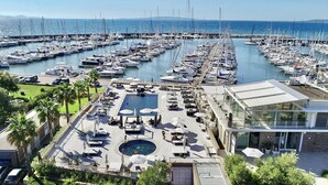 A marina with numerous boats docked, a swimming pool, and a modern building with outdoor seating.