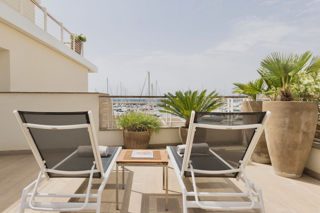 Een balkon met twee witte lounge fauteuils, een tafeltje en potplanten.