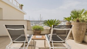 A balcony with two white lounge chairs, a small table, and potted plants.