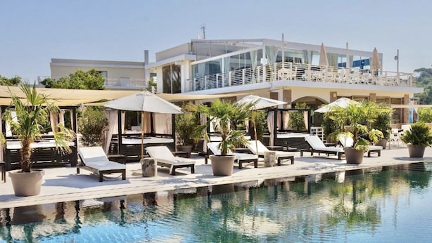 A poolside area with lounge chairs and umbrellas, a modern building in the background, and a clear blue pool.