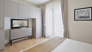 A modern bedroom with a bed, a TV on a grey cabinet, and a framed picture on the wall.