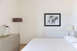 Habitación de hotel minimalista con cama, cómoda, lámpara y un cuadro en la pared.
