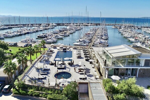 Un puerto deportivo con numerosas embarcaciones amarradas, una piscina y un edificio moderno con terraza.