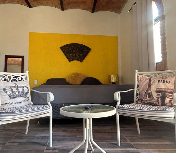 A bedroom with a bed, two chairs, a small table, and a decorative wall piece.