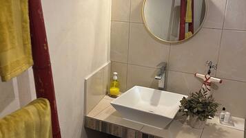A bathroom with a white sink, a round mirror, a towel rack, a small plant, and a bottle of soap.