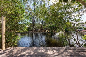 Relax on the deck overlooking the calm water, surrounded by lush greenery and trees.