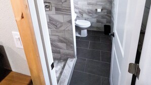 Un baño con inodoro, ducha y piso de baldosas.