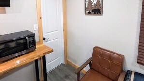 Habitación pequeña con aire acondicionado blanco, puerta de madera, sillón de cuero marrón y un pequeño adorno en la pared.