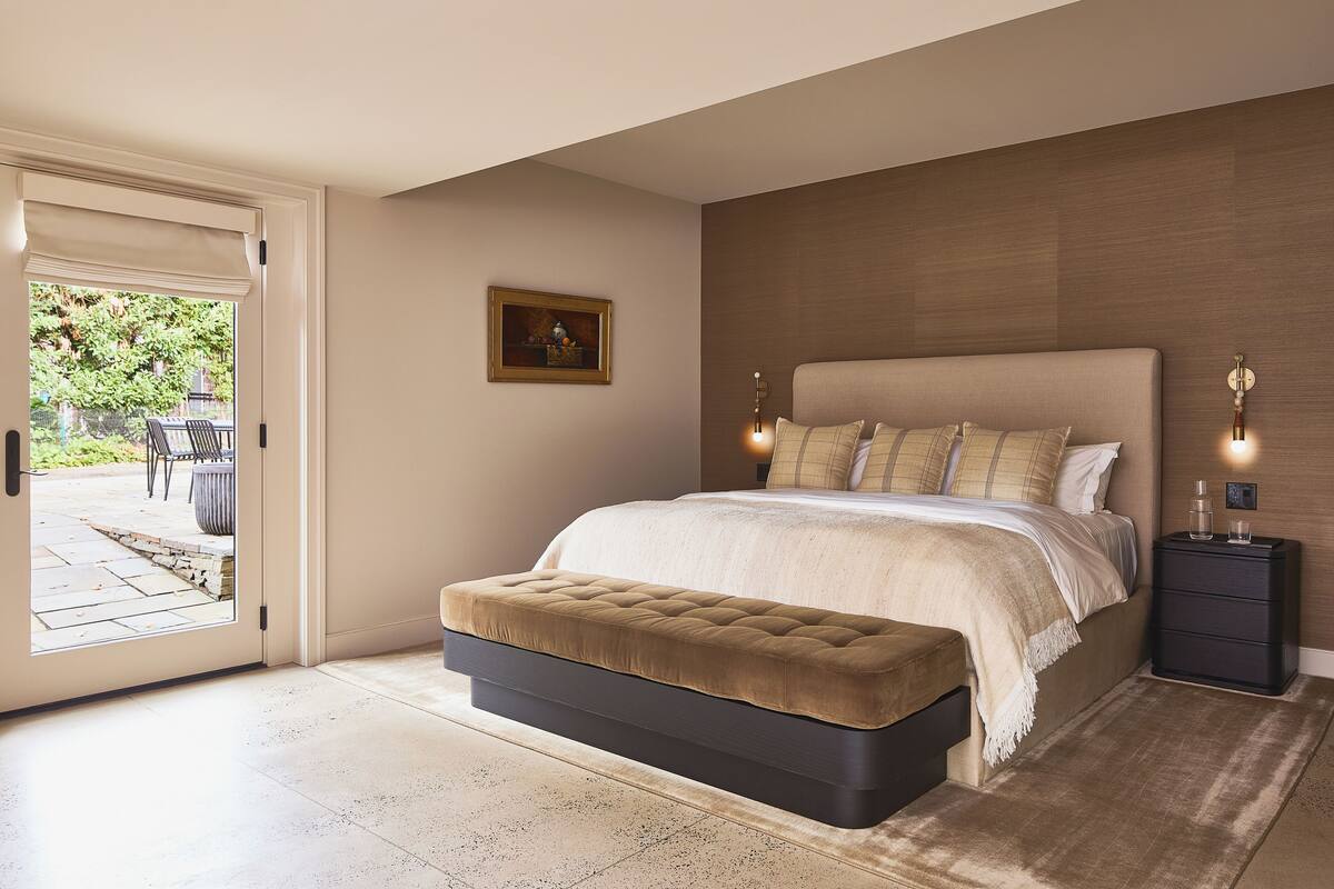 Ein Schlafzimmer mit einem großen Bett, einer Sitzbank, einem Nachttisch und einer Tür, die auf eine Terrass führt.
