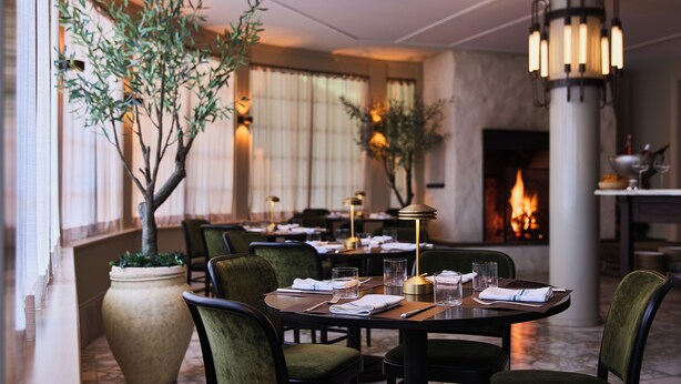 A dining area with round tables, green upholstered chairs, and a large potted plant. - Stockton Inn (Stockton)