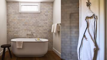 Un baño con una bañera independiente, un taburete pequeño, un perchero y una ventana sobre la bañera.