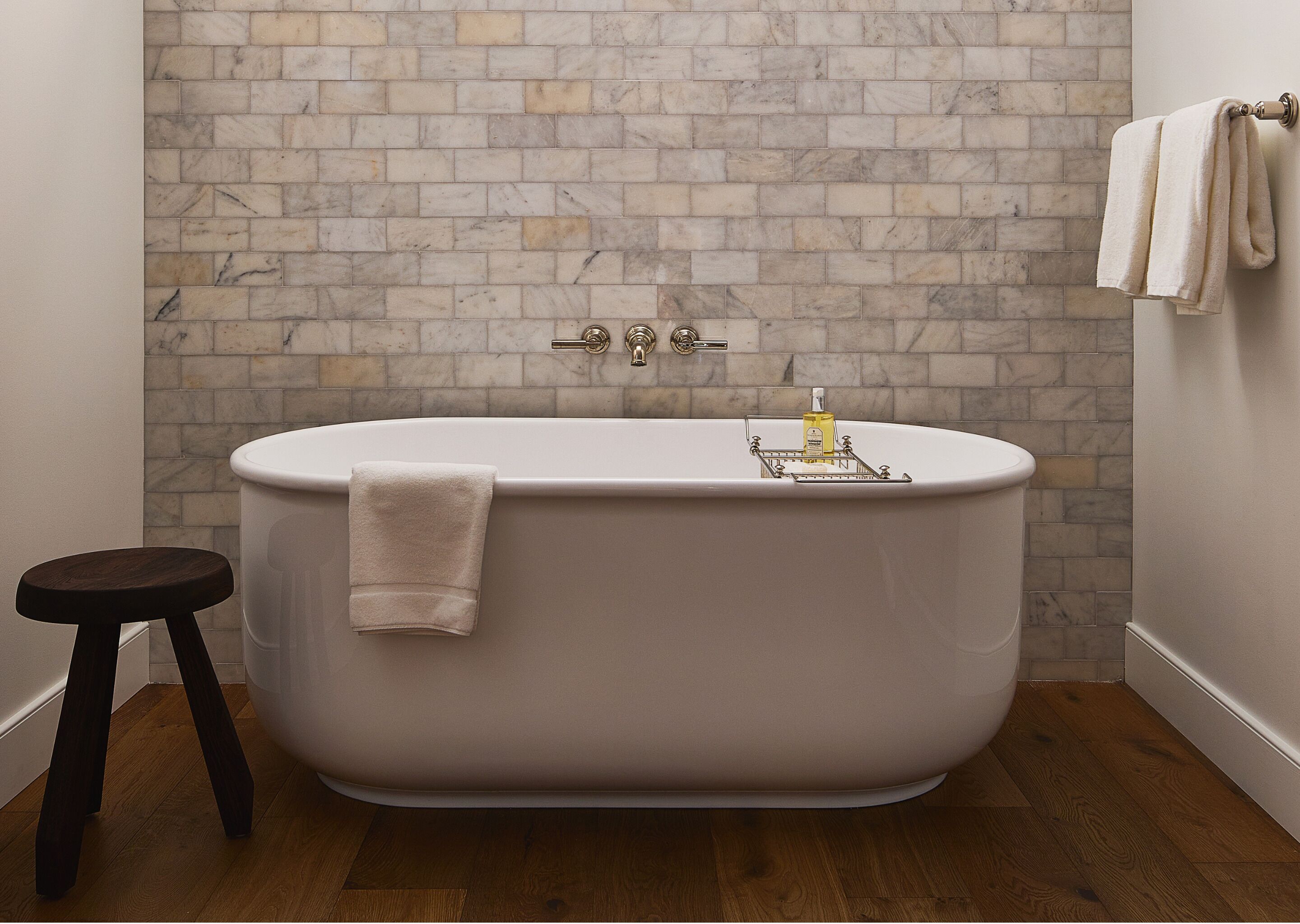 A bathroom with a freestanding bathtub, a wooden stool, and a marble-patterned wall.