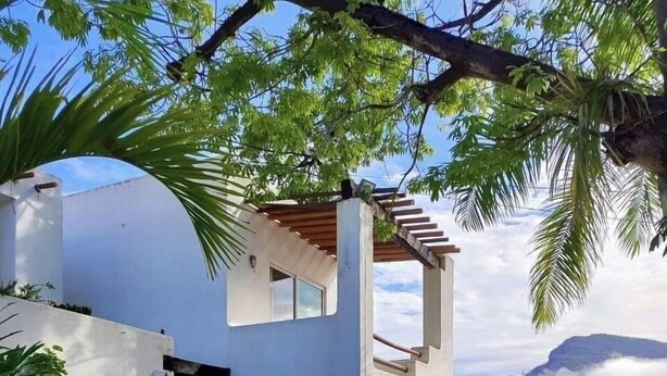 A modern two-story house with a covered patio, surrounded by lush greenery and a mountain backdrop. - Bungalows Adelamar (Zihuatanejo)