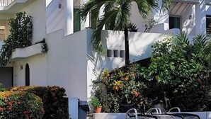 A modern building with a pool, surrounded by lush greenery and palm trees. - Bungalows Adelamar (Zihuatanejo)