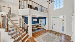 Un hall d’entrée spacieux avec un escalier en bois, un coin repas et une grande fenêtre qui laisse entrer la lumière naturelle.