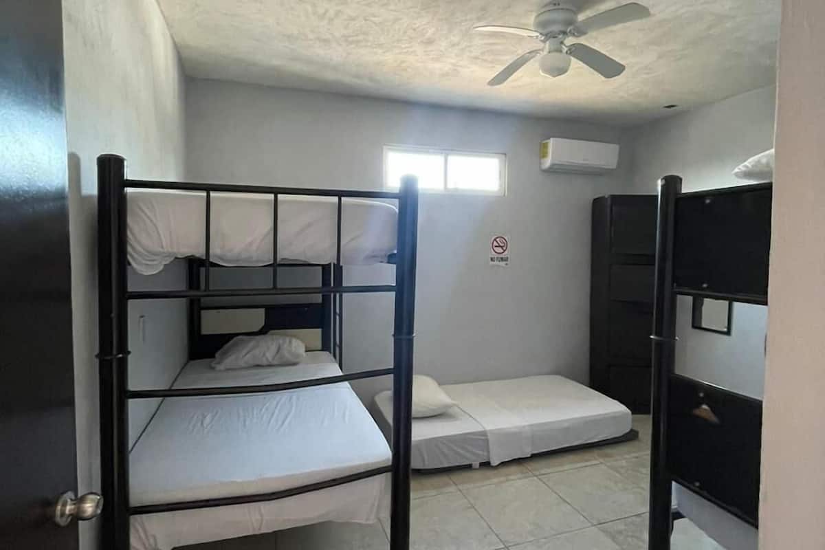 A dormitory room with bunk beds, a ceiling fan, and a window.