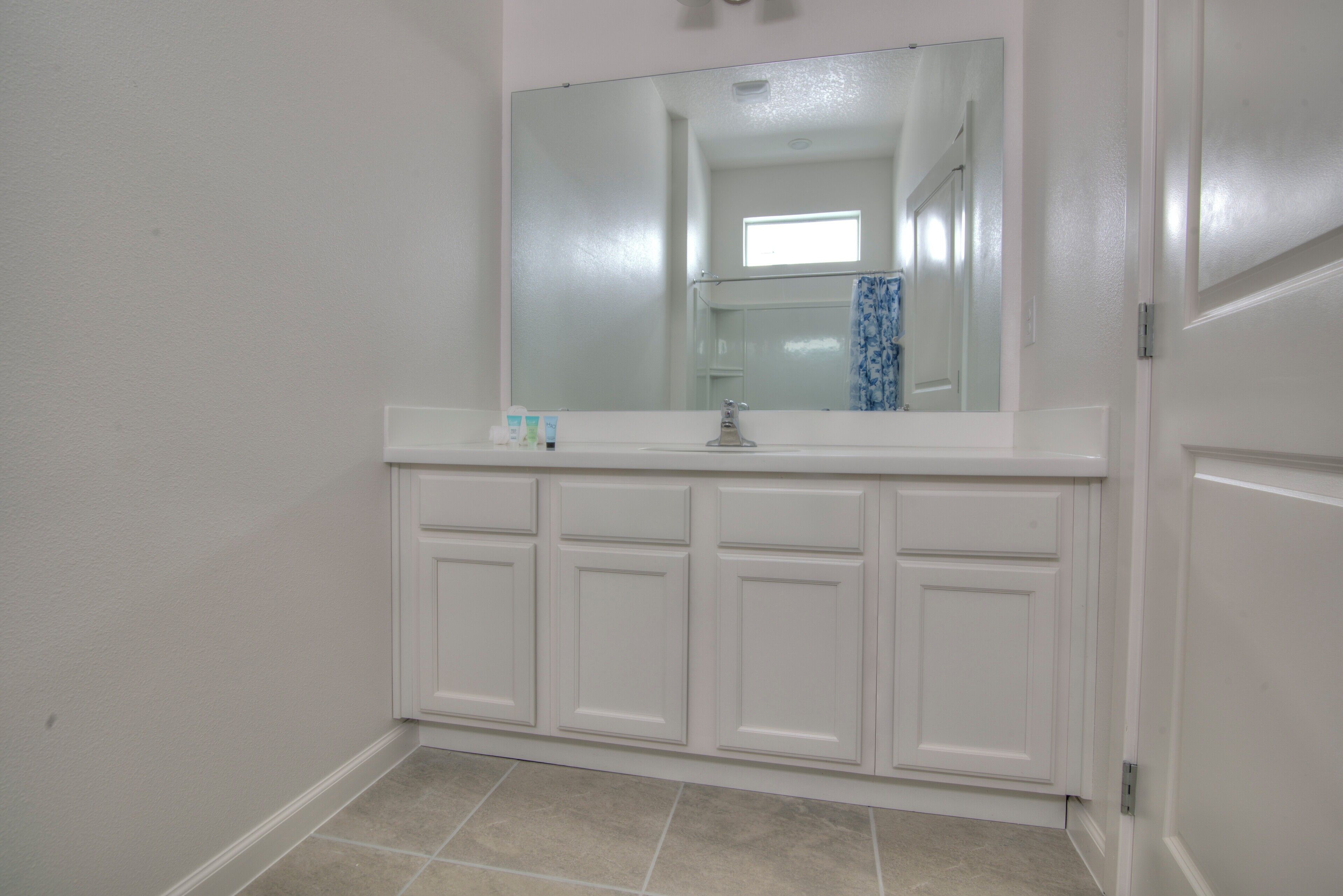 A bathroom with a white vanity, a mirror, and a tiled floor.