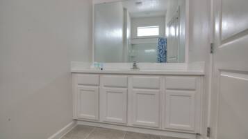A bathroom with a white vanity, a mirror, and a tiled floor.