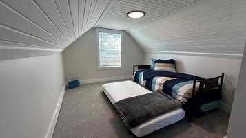 A small, sloped ceiling room with two beds, a window, and a blue storage bin.