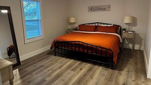 Une chambre à coucher comprenant un lit, deux tables de chevet, un ventilateur de plafond, une fenêtre avec des stores et un panneau décoratif mural.