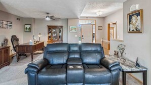 A living room with a black leather sofa, a wooden desk, and a ceiling fan. - Charming 2-bedroom house in lovely Omaha with AC, WiFi. (Omaha)