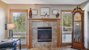 A living room with a fireplace, framed pictures, a clock, and a view of the outdoors. - Charming 2-bedroom house in lovely Omaha with AC, WiFi. (Omaha)