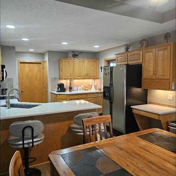 A compact kitchen with wooden cabinets, a refrigerator, a coffee maker, and a dining area with a table and chairs.