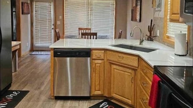 A modern kitchen with wooden cabinets, a stainless steel dishwasher, and a large island with a sink. - Charming 2-bedroom house in lovely Omaha with AC, WiFi. (Omaha)