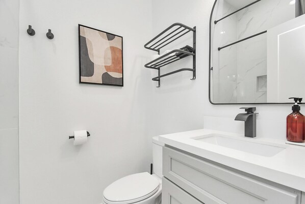 A modern bathroom with a white vanity, a toilet, a towel rack, a sink, and a mirror.