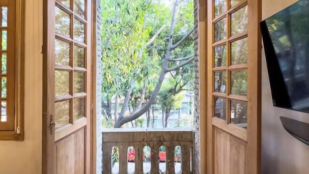 A hallway with a wooden door leading to a balcony with a view of trees. - Lasai Casa Puebla  (Mexico City)