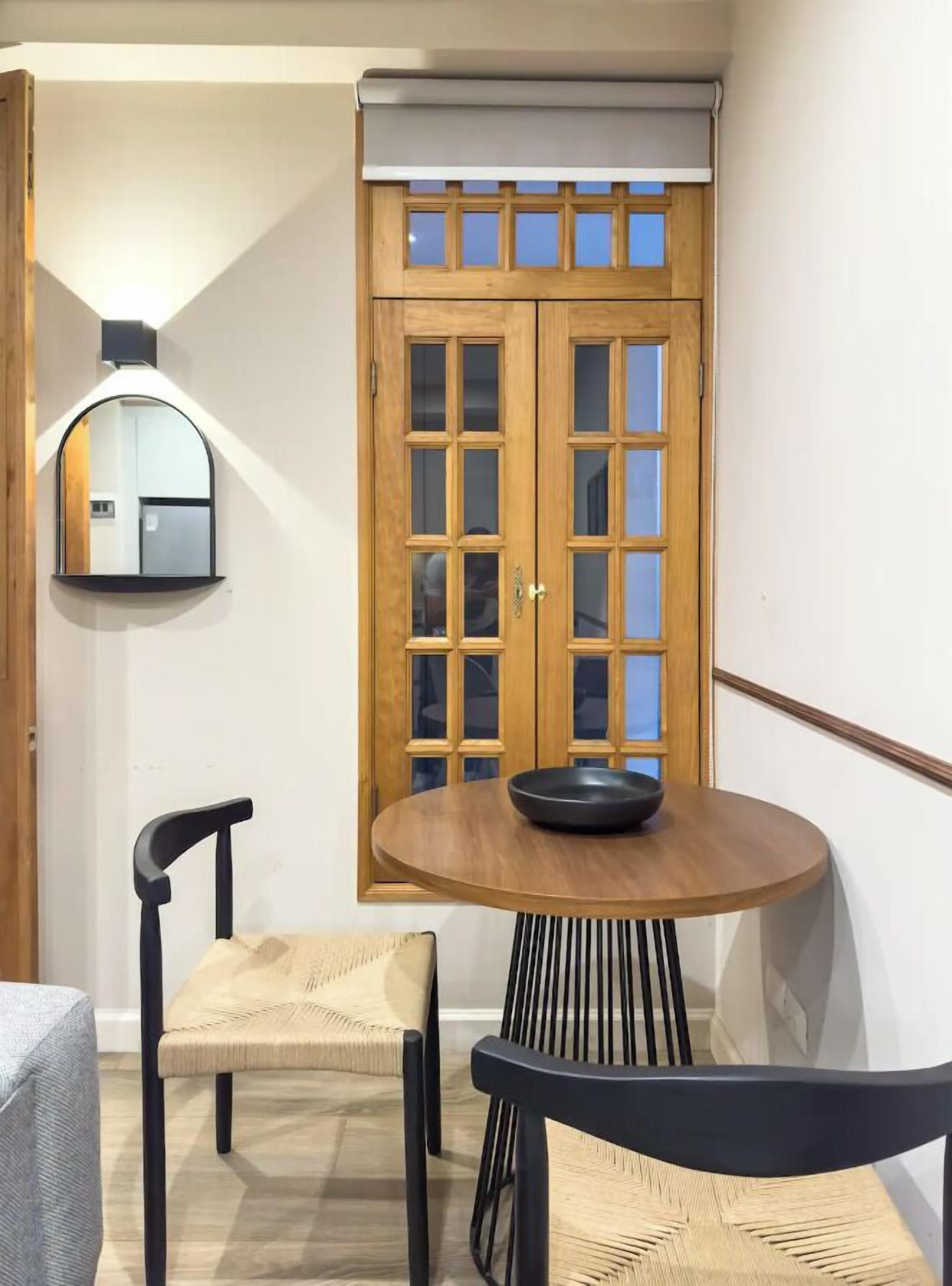 A room with a round wooden table, two chairs, a mirror, and a wooden door with glass panels.