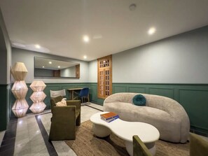 A modern living room with a beige sofa, a coffee table, and a blue chair. There is a large mirror on the wall, a wooden door, and a lamp with a geometric design. - Lasai Casa Puebla  (Mexico City)