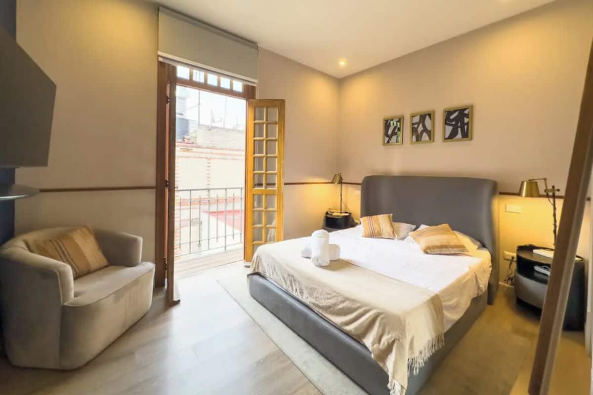 A modern bedroom with a large bed, a sofa, and a balcony with a view.