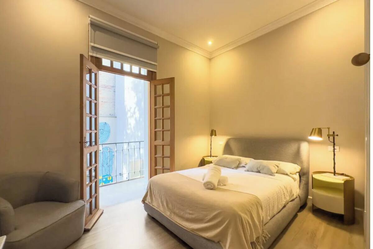 A bedroom with a bed, bedside tables, a sofa, and a balcony.