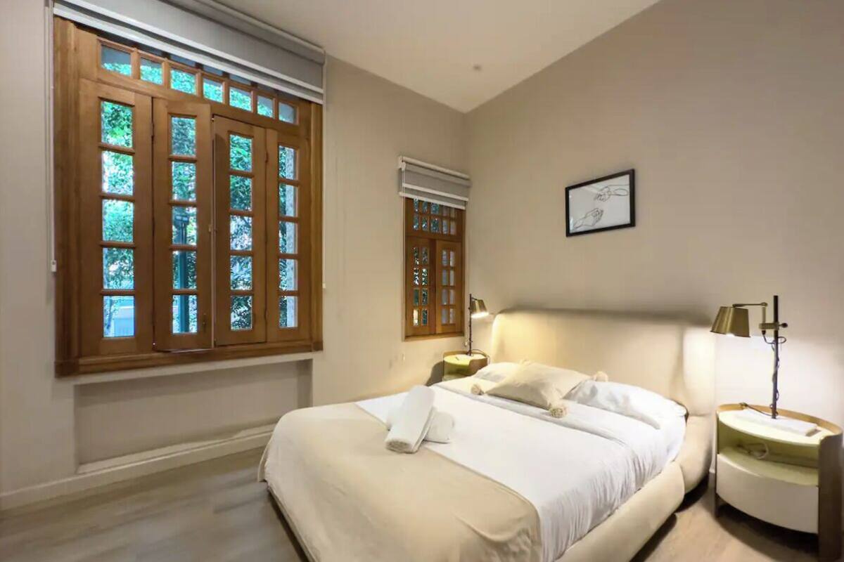 A bedroom with a large bed, two bedside tables, a window with wooden shutters, and a framed picture on the wall.