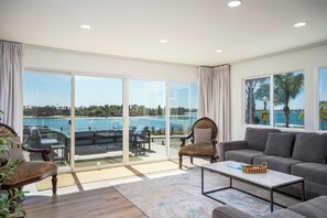 A spacious living room with a large sliding glass door leading to a balcony overlooking a body of water. - Pacific Beach Bayfront w/Captivating Views 5BR/5BA POOL HotTub Fire Table BBQ AC (San Diego)