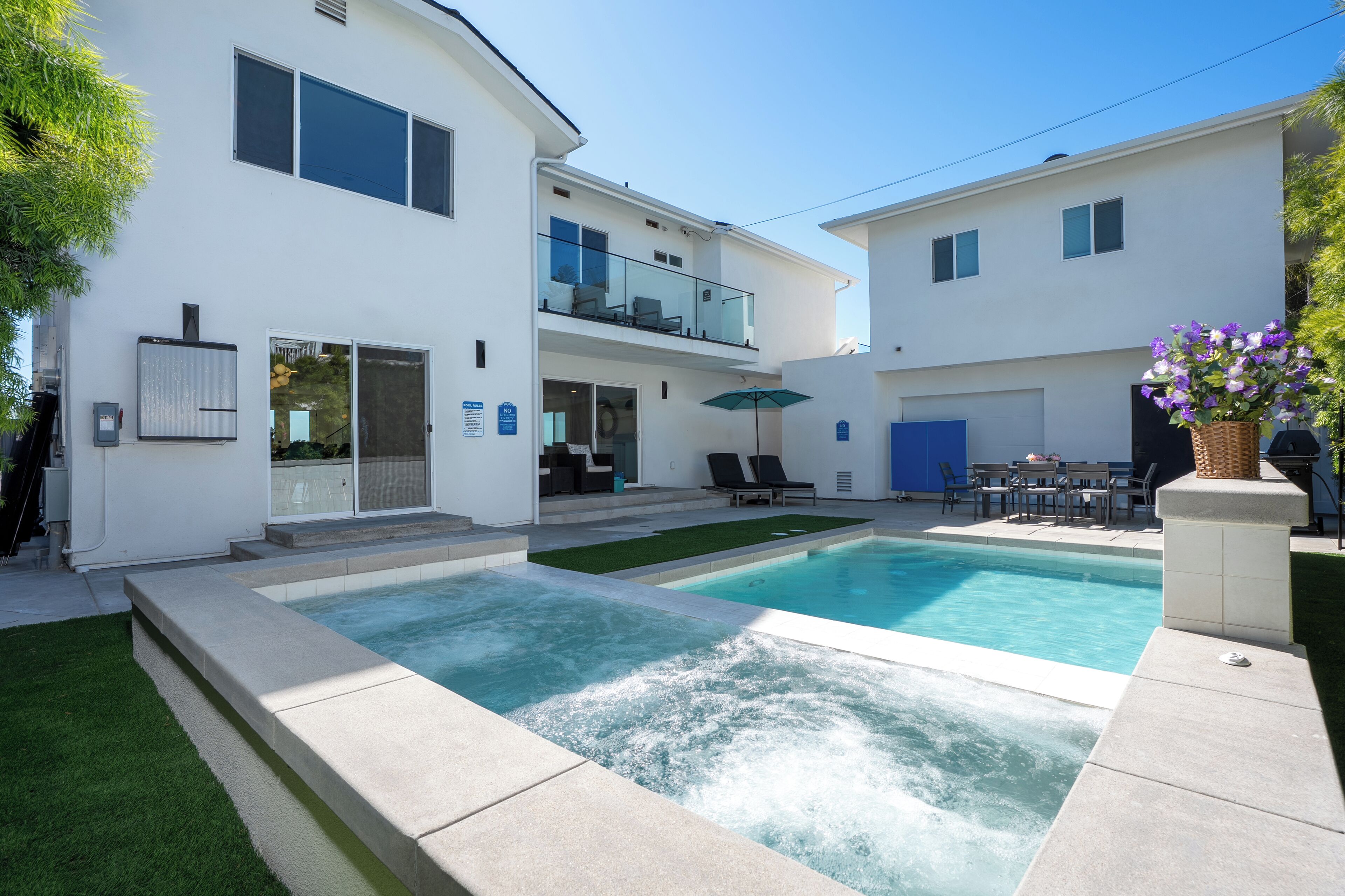 A modern two-story house with a swimming pool, a balcony, and a patio area with outdoor furniture.