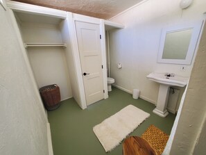 Compact bathroom with a white toilet, sink, and mirror, plus a green mat and white rug.