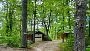 A forested area with a dirt path leading to a small cabin with a garage.