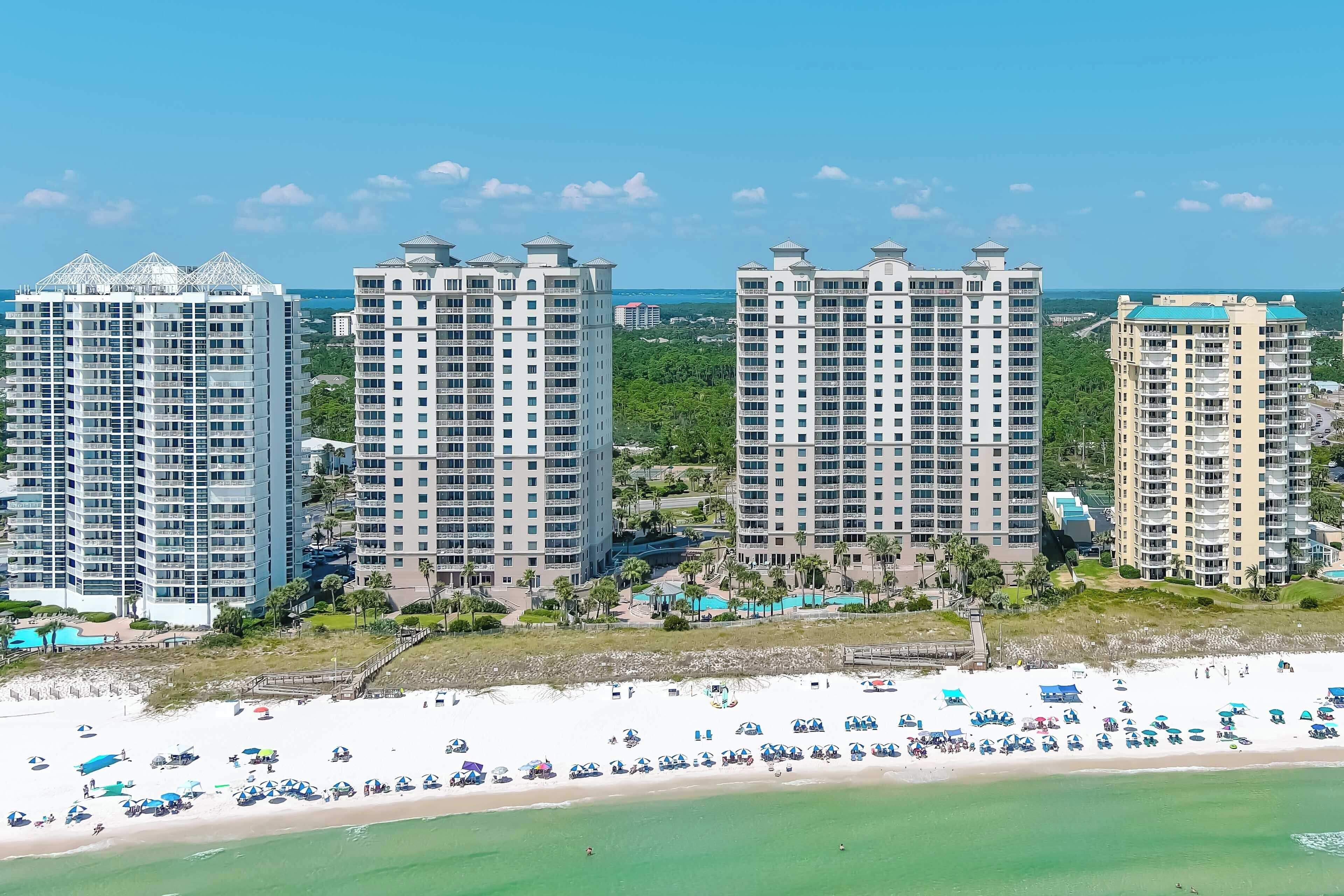A beachfront hotel with multiple high-rise buildings, a sandy beach, and a clear blue sky.