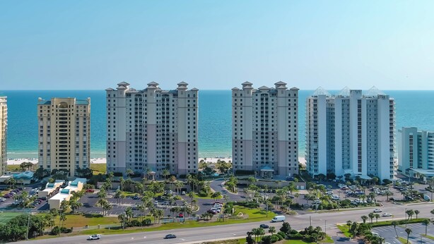 Un hotel moderno a la orilla del mar, con varios pisos, estacionamiento y vistas al océano.